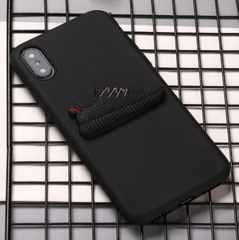 Puede incluir: Funda de tel&eacute;fono negra con una zapatilla negra 3D unida a la parte posterior.