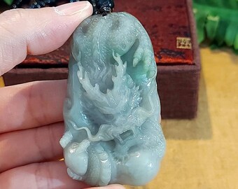 May include: A jade pendant carved with a detailed dragon design. The pendant is a light green color and has a black cord attached to it.