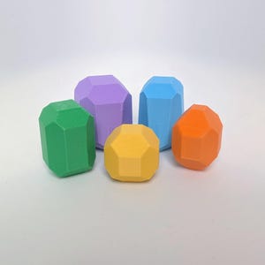 May include: Five colourful, geometric, faceted, gemstone-shaped toys. The toys are made of plastic and are in the colours green, purple, blue, orange, and yellow.
