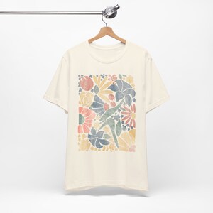 May include: A cream colored t-shirt with a colorful floral print. The print features a variety of flowers and leaves in shades of yellow, orange, pink, blue, and green.