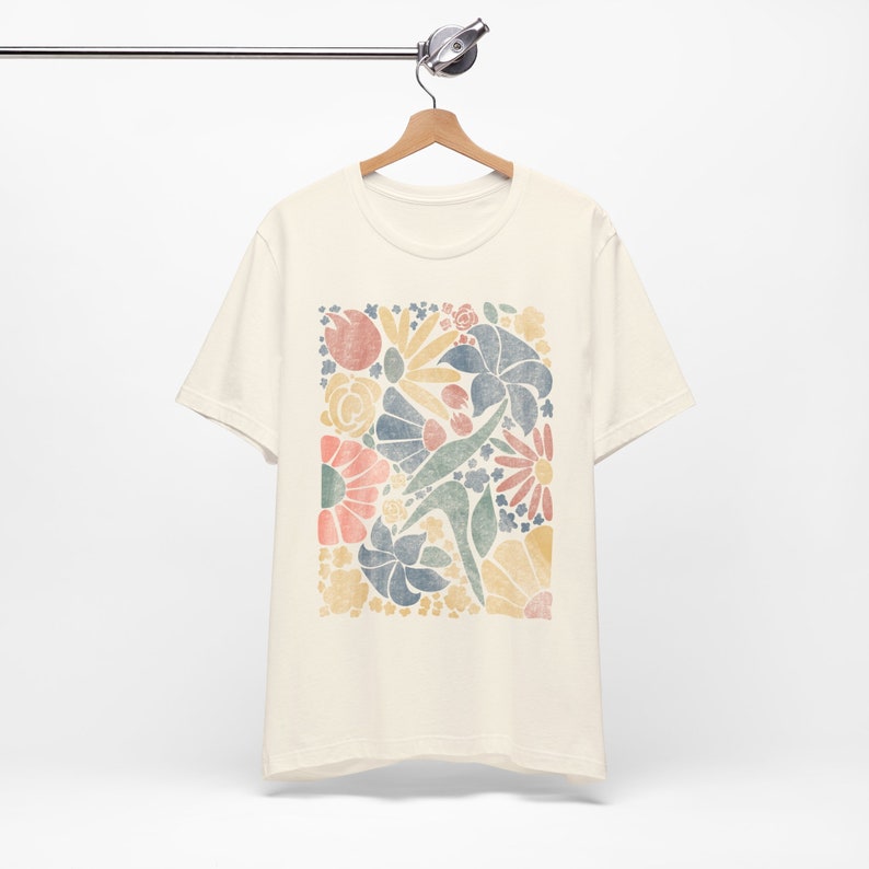 May include: A cream colored t-shirt with a colorful floral print. The print features a variety of flowers and leaves in shades of yellow, orange, pink, blue, and green.