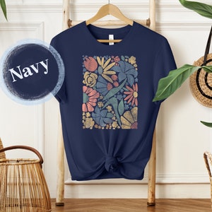 May include: A navy blue t-shirt with a colorful floral print. The print features a variety of flowers and leaves in shades of pink, yellow, green, and blue.