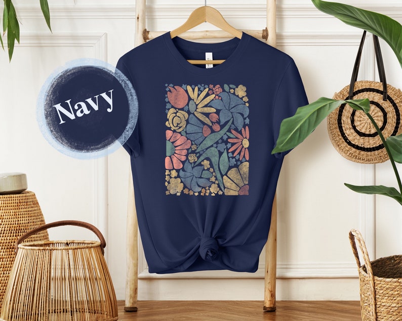 May include: A navy blue t-shirt with a colorful floral print. The print features a variety of flowers and leaves in shades of pink, yellow, green, and blue.