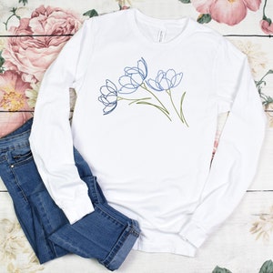 May include: White long-sleeve t-shirt with a blue line drawing of three flowers on the front.