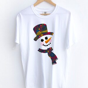 Puede incluir: Camiseta blanca con un gr&aacute;fico de mu&ntilde;eco de nieve colorido. El mu&ntilde;eco de nieve tiene un sombrero y una bufanda con estampado floral.