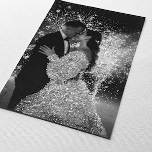 May include: Black and white photograph of a couple kissing, with a sparkling effect overlay. The woman wears a textured, embellished gown. The man is in a tuxedo. The image is printed on a rectangular card.