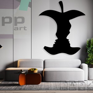 May include: A black silhouette of a bitten apple with two faces inside, on a white wall in a modern living room with a grey sofa, a coffee table, and a potted plant.