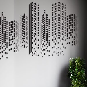 May include: A black and white cityscape wall decal with a modern design. The decal features a series of buildings made up of small squares. The decal is perfect for adding a touch of urban style to any room.