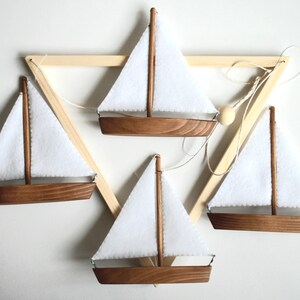 Puede incluir: Cuatro veleros de madera con velas de tela blanca colgando de un marco triangular de madera. Los veleros est&aacute;n suspendidos por cuerdas y todos est&aacute;n orientados en la misma direcci&oacute;n.