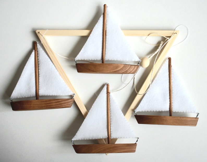 Puede incluir: Cuatro veleros de madera con velas de tela blanca colgando de un marco triangular de madera. Los veleros est&aacute;n suspendidos por cuerdas y todos est&aacute;n orientados en la misma direcci&oacute;n.