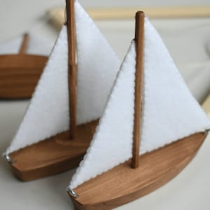 Puede incluir: Dos veleros de madera con velas de tela blanca. Los veleros est&aacute;n colgados de un marco de madera.