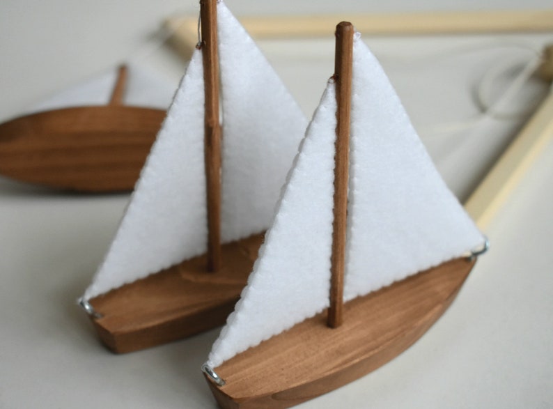 Puede incluir: Dos veleros de madera con velas de tela blanca. Los veleros est&aacute;n colgados de un marco de madera.