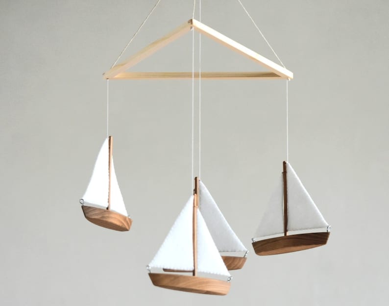 Puede incluir: Un m&oacute;vil de madera con tres veleros blancos colgando de un marco triangular de madera. Los veleros est&aacute;n hechos de madera y tienen velas de tela blanca.