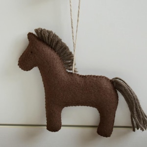May include: A brown felt horse ornament with a brown mane and tail, hanging from a string. The horse is a simple, stylized design, perfect for nursery decor or a rustic touch to any room.