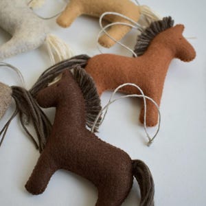 May include: Handmade felt horse ornaments in various shades of brown, tan, and cream. Each horse has a yarn mane and tail, and a string for hanging. These rustic ornaments are perfect for a country-themed Christmas tree or as a gift.