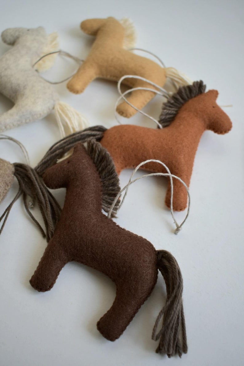 May include: Handmade felt horse ornaments in various shades of brown, tan, and cream. Each horse has a yarn mane and tail, and a string for hanging. These rustic ornaments are perfect for a country-themed Christmas tree or as a gift.