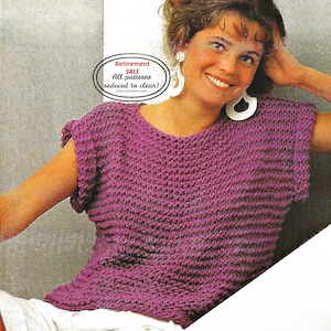 May include: A short-sleeved, V-neck knit top in a deep purple hue. The top has a textured, horizontal ribbing pattern. A small oval graphic in the upper left corner reads "Retirement SALE All patterns reduced to clean!" in white text.