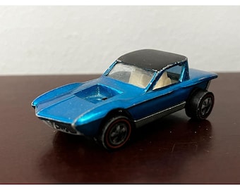 May include: A blue toy car with a black roof and a white interior. The car has a long, low profile and a distinctive design. It is a vintage Hot Wheels car.
