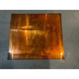 May include: A rectangular copper sheet with a textured surface and a light brown color. The sheet has a slightly reflective surface and appears to be slightly warped.