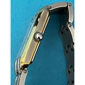 May include: A rectangular wristwatch with a silver band and a gold-toned bezel. The watch face is a light blue color. The watch has a silver crown and a silver clasp. The watch is a classic design.