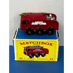 May include: Red Matchbox toy fire truck with "Airport Crash Tender" printed on the side. The truck is in its original box, which has the Matchbox logo and the words "A Lesney Product".