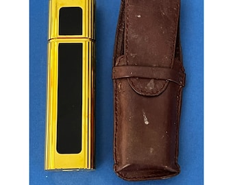 May include: A gold-colored lighter with a black insert and a brown leather case.
