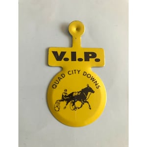 May include: Yellow metal VIP pass for Quad City Downs with a black silhouette of a horse and driver. The pass has a hole at the top for hanging.