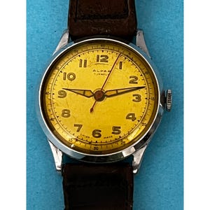 May include: Vintage ALPAR watch with a silver case, a yellow dial, and a brown leather strap. The watch face features black numerals and hands, with the text "ALPAR 7 JEWEL SWISS MADE".