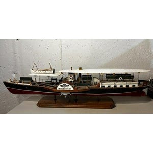 May include: A detailed model of a paddle steamer boat, featuring a black hull with red accents and a white upper deck. The model includes a small lifeboat, benches, and the name "Hercules" on the front. It sits on a wooden base.