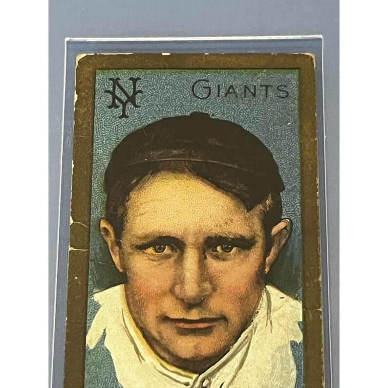 K&ouml;nnte beinhalten: Eine Vintage-Baseballkarte mit einem Nahaufnahmeportr&auml;t eines Baseballspielers mit einer Kappe. Die Karte hat einen blauen Hintergrund mit dem Text "Giants" und einem New York Giants-Logo in der oberen linken Ecke.