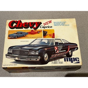 May include: A model kit box for a Chevy Caprice. The box features a black car with red and white accents, and the text "National Street Rod Association." The box also shows a blue car and a trailer.