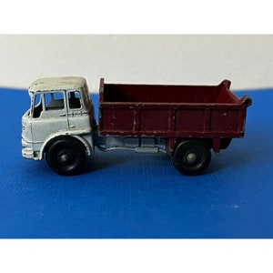 May include: A white toy dump truck with a red bed. The truck has a detailed cab with a windshield and two doors. The truck has four wheels and a black chassis.