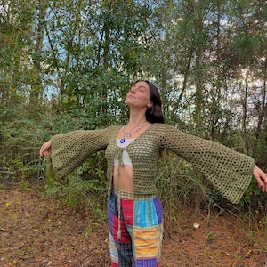 K&ouml;nnte beinhalten: Eine Frau tr&auml;gt ein gr&uuml;nes H&auml;keltop mit Glocken&auml;rmeln und eine bunte Patchworkhose. Sie steht in einem Wald mit gr&uuml;nen B&auml;umen und braunen Bl&auml;ttern auf dem Boden.