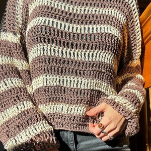 Puede incluir: Un su&eacute;ter de crochet a rayas marrones y crema con un corte holgado y mangas largas.