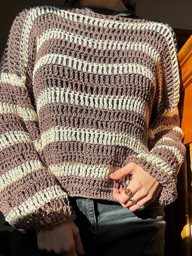 Puede incluir: Un su&eacute;ter de crochet a rayas marrones y crema con un corte holgado y mangas largas.
