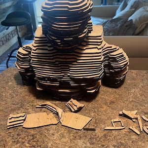 Puede incluir: Un modelo de madera del torso de una persona, hecho de muchas capas de madera, está ensamblado en una encimera marrón. El modelo está sin terminar y tiene varias piezas de madera alrededor.