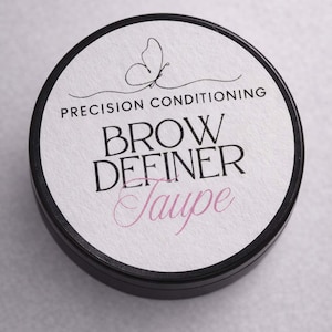 May include: A black circular container with a white label. The label has the text "PRECISION CONDITIONING BROW DEFINER Taupe" and a butterfly illustration. The product is for eyebrow definition.