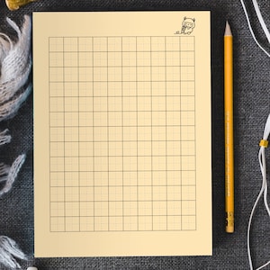 Puede incluir: Un papel cuadriculado de color crema con una pequeña ilustración de dibujos animados en la esquina superior derecha. Un lápiz amarillo descansa en el lado derecho del papel. El papel está sobre una superficie gris.
