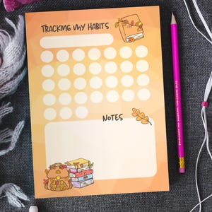 May include: A habit tracker with the text "Tracking My Habits" and "Notes" on an orange and yellow gradient background. The tracker has a series of circles for marking habits. A pink pencil and decorative illustrations of books and a backpack are also visible.