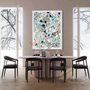 May include: An abstract art print in a silver frame hangs above a dining table. The artwork features a mix of blue, beige, black, and gray colors. The dining set includes a round table, four black chairs, and decorative items.