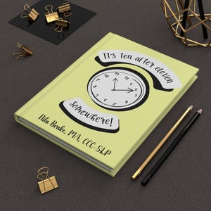 May include: A light yellow hardcover journal featuring a central clock illustration with black hands. The text reads It's ten after eleven somewhere! and Nita Brake, MA, CCC-SLP. The cover design includes white banners above and below the clock graphic.
