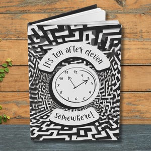 May include: A notebook with a black and white maze design. The cover features a clock graphic with the text "It's ten after eleven somewhere!" The clock hands point to 2:10. The notebook is open, revealing white pages.
