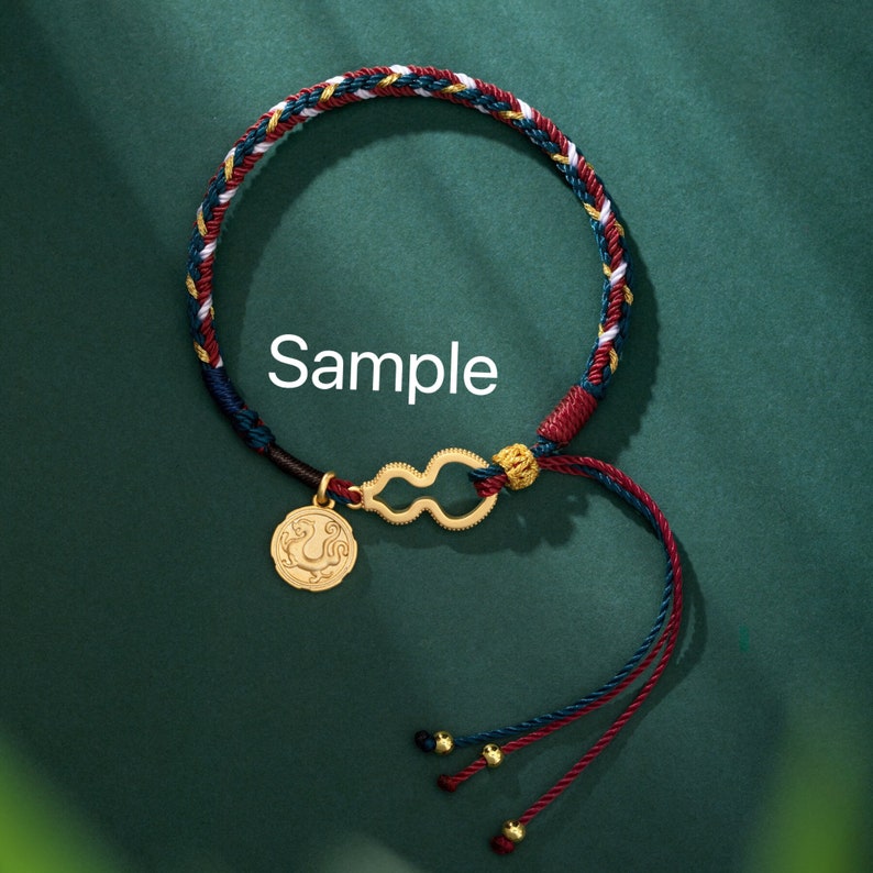 May include: Braided bracelet with red, blue, white, and gold threads. The bracelet features a gold-colored charm with a coin-like pendant and a gourd-shaped connector. The word "Sample" is printed on the image.