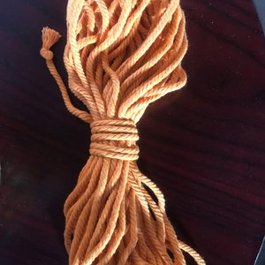 K&ouml;nnte beinhalten: Nahaufnahme eines orangefarbenen Seils, das aufgerollt ist. Das Seil ist etwa 3 Meter lang und aus Naturfasern hergestellt. Das Seil ist oben in einem Knoten gebunden. Der Text "Actual size of one unit" ist im Bild sichtbar.