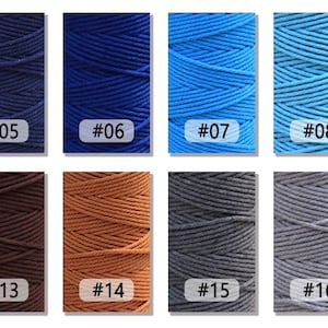 K&ouml;nnte beinhalten: Nahaufnahme von acht Spulen mit Baumwollschnur in verschiedenen Farben, darunter Marineblau, K&ouml;nigsblau, Hellblau, Himmelblau, Braun, Beige, Grau und Anthrazit. Jede Spule ist mit einer Nummer gekennzeichnet.