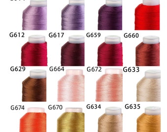Könnte beinhalten: Eine Sammlung von 24 Spulen Stickgarn in verschiedenen Farben, darunter Rosa, Rot, Orange, Gelb, Braun und Lila. Jede Spule ist mit einem eindeutigen Code gekennzeichnet, wie z. B. G601, G614, G629, G674, G607 und G667.