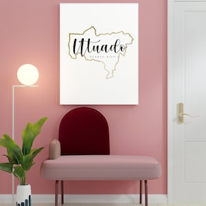 May include: A white canvas print with a gold outline of the island of Puerto Rico and the word "Utuado" in black script. The print is hanging on a pink wall above a pink and burgundy chair.
