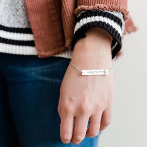 Peut inclure: Un bracelet en chaîne argent avec un charme rectangulaire qui dit "אף  לי  איתך  אהבה" en hébreu.