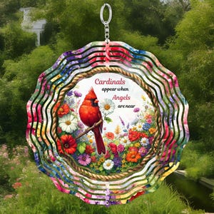 May include: A decorative wind spinner featuring a vibrant red cardinal perched on a branch, surrounded by colorful flowers. The text reads "Cardinals appear when Angels are near." The spinner has a floral patterned border and a silver hanging loop.
