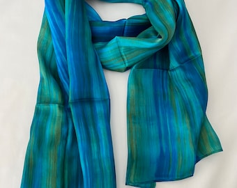 May include: A blue and green striped silk scarf. The scarf is folded in half and laid flat on a white surface.